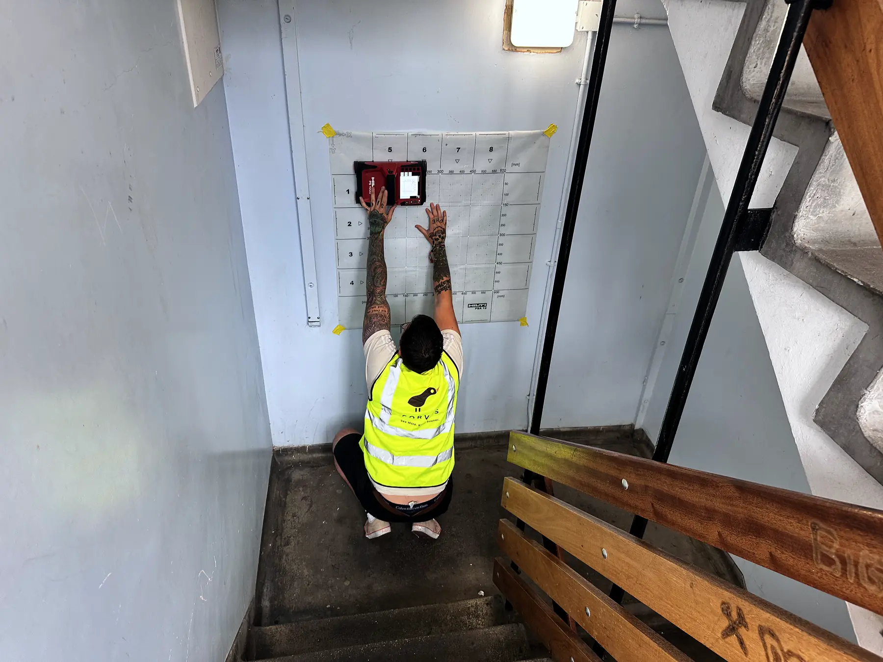 Corvus surveyor scanning a stairwell wall through a grid sheet in an occupied high-rise block in East London